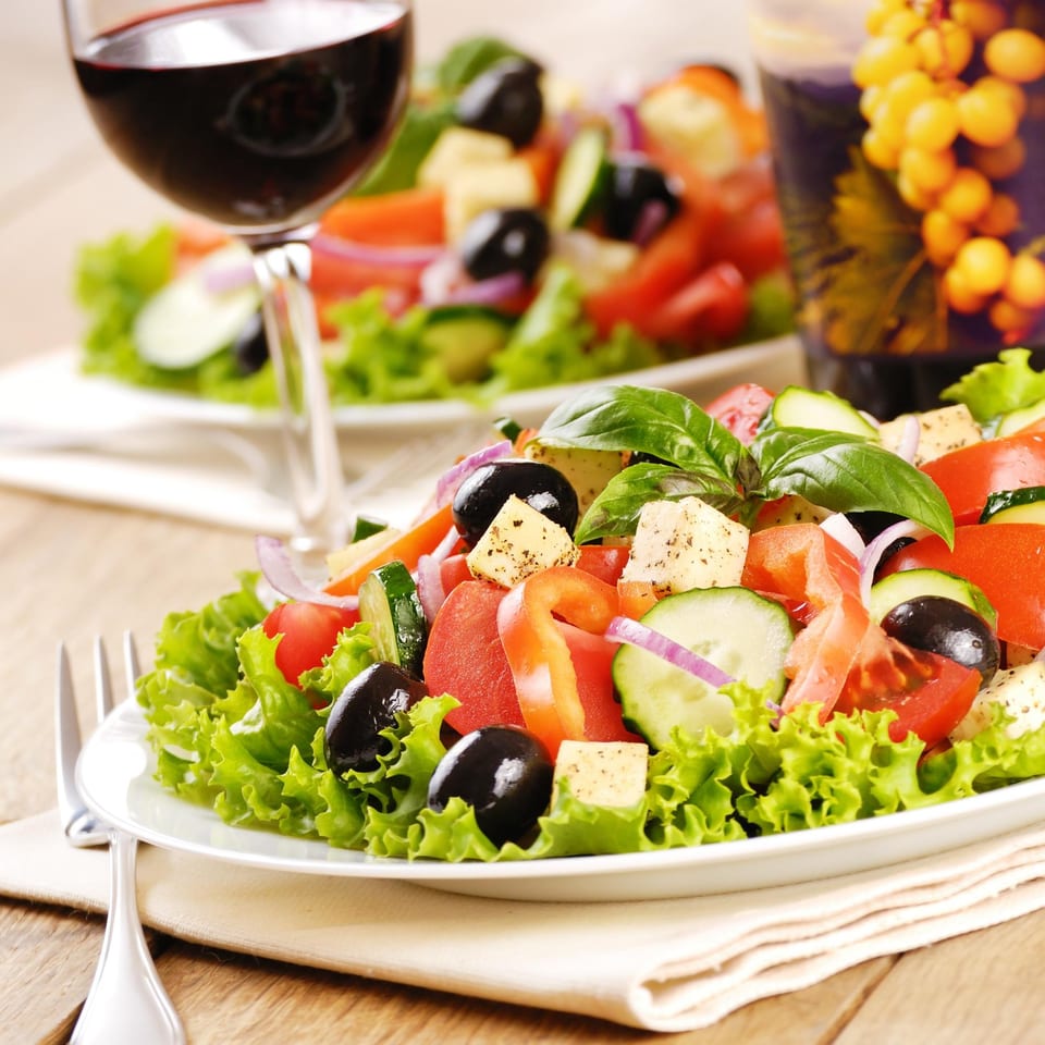 Two fresh Greek salads with feta, olives, and vegetables, served with red wine.
