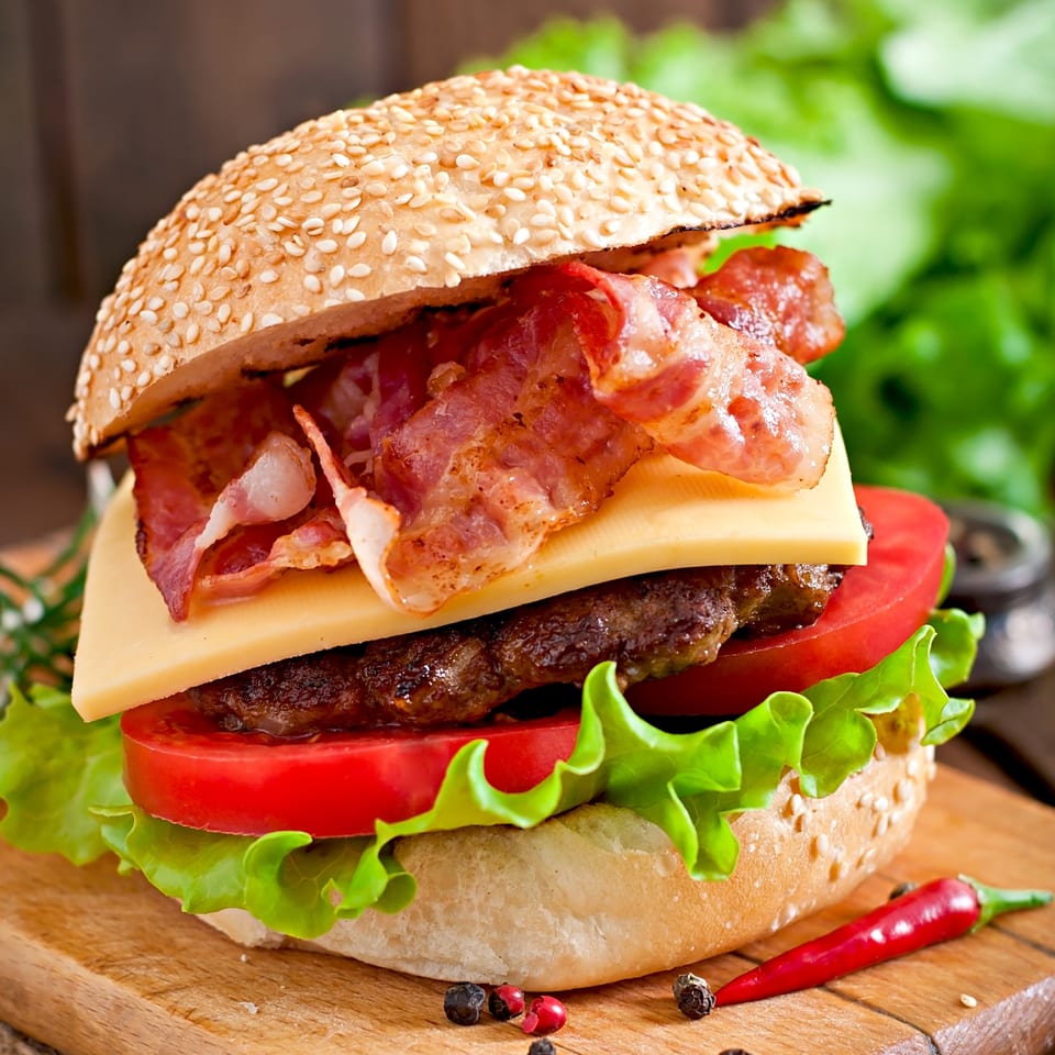 A close-up of a bacon cheeseburger with lettuce and tomato on a wooden board.