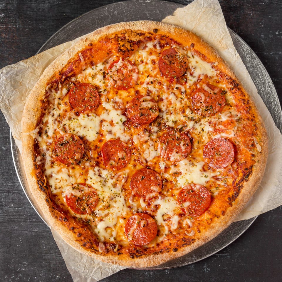 A freshly baked pepperoni pizza from Pizza 24, topped with cheese and herbs on parchment paper.